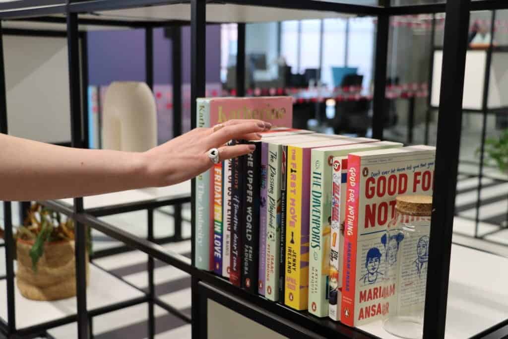 Hand with jewellery reaching for book shelf, with seven colourful books in a row.